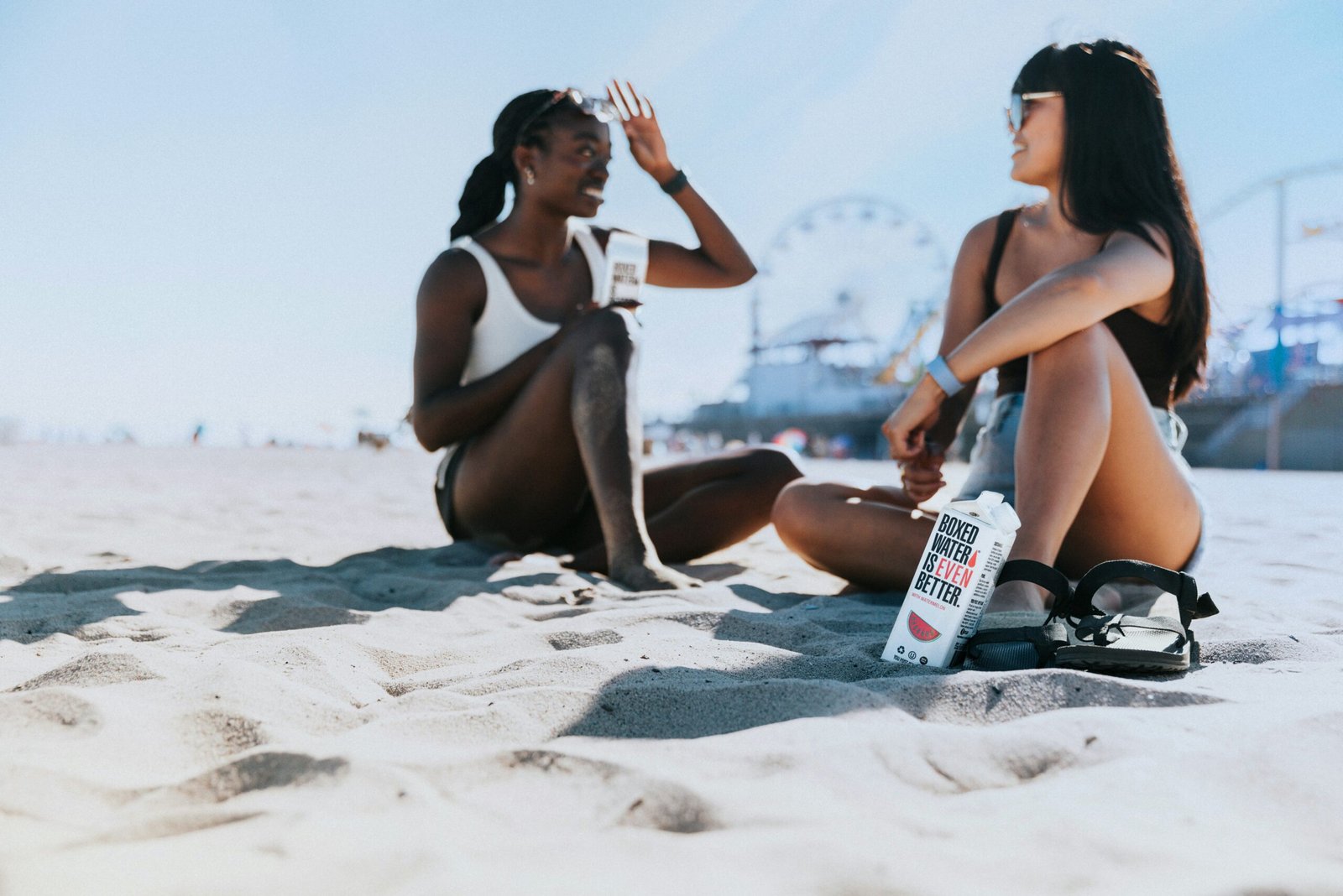 two women sitting in the sand at the beach